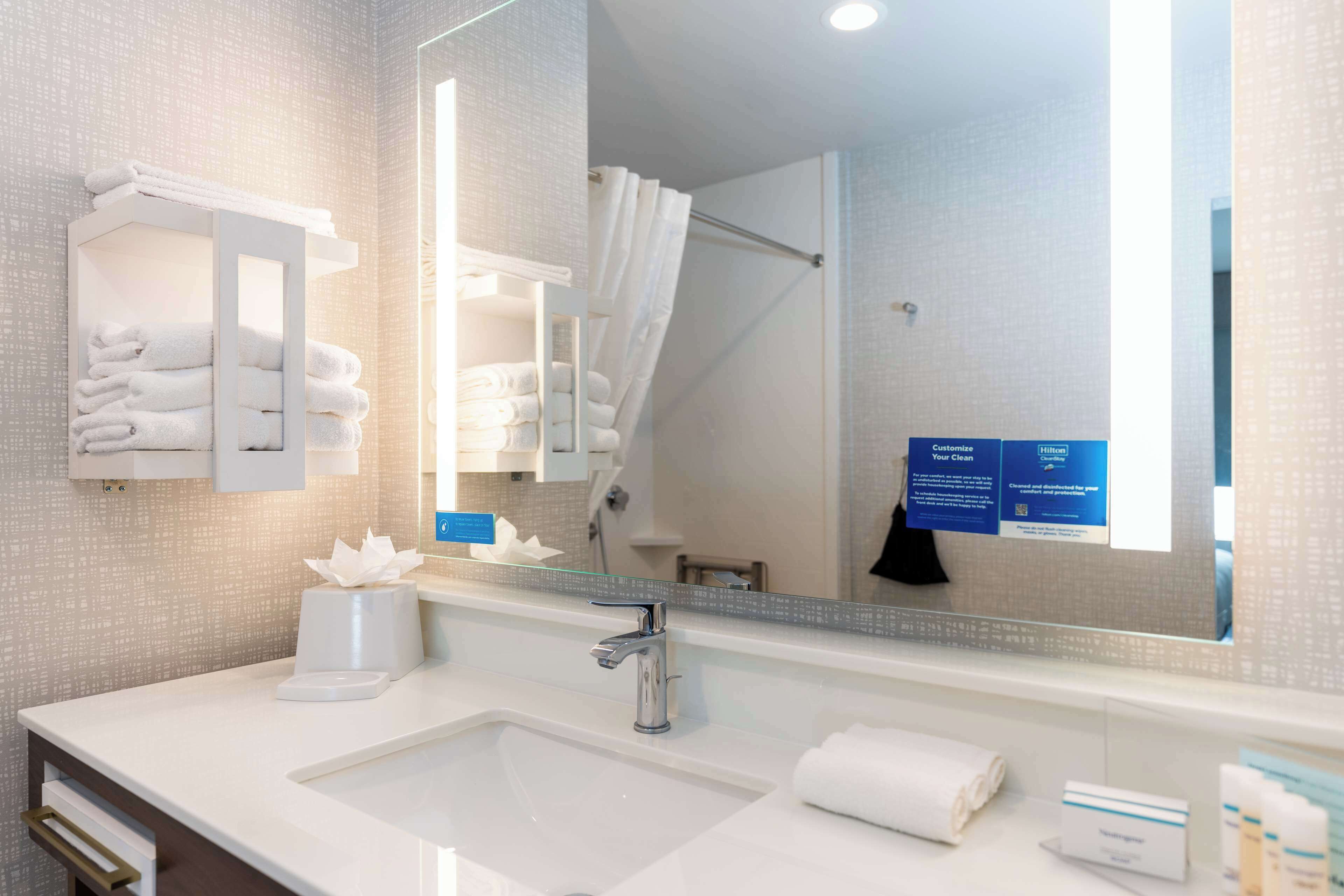 Une salle de bain moderne avec un grand miroir, un lavabo blanc et un espace de rangement pour les serviettes.