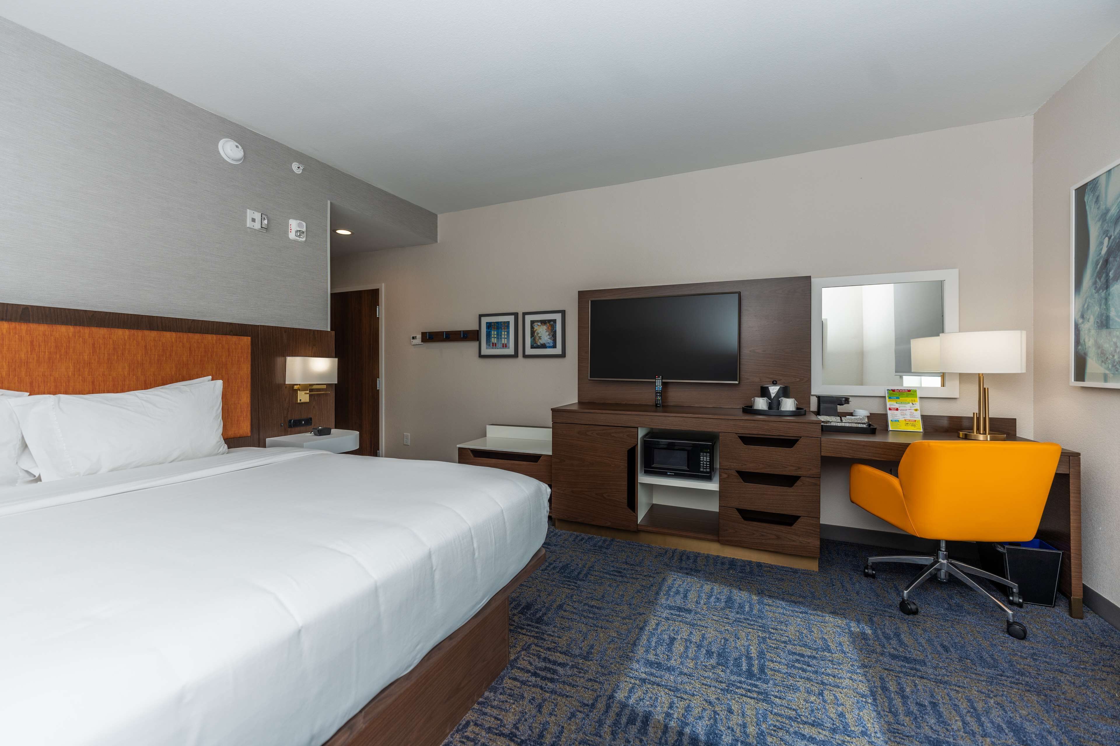 A hotel room with a large bed, a desk with a computer, a television, and a chair.
