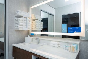 A modern bathroom with a large mirror, white sink, and neatly stacked towels.
