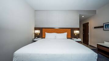 Habitación de hotel con una cama grande, mesitas de noche con lámparas, cabecera de madera, un pequeño escritorio y un cuadro en la pared.
