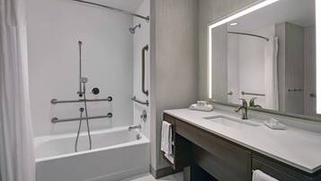Un baño moderno con ducha a ras de suelo, barras de apoyo, un espejo grande y un mueble de tocador con lavabo.