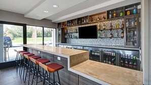 A modern bar area with a long counter, multiple stools, and a variety of liquor bottles.