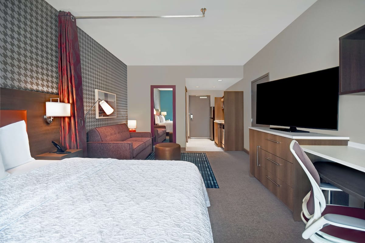 Habitación de hotel moderna con una cama grande, un escritorio, un televisor y un baño visible a través de una puerta abierta.