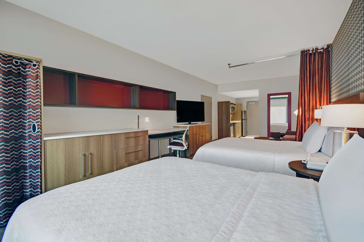 Habitación de hotel con dos camas, un escritorio, televisor y baño con cortina de ducha.