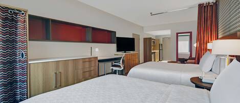 A hotel room with two beds, a desk, a television, and a bathroom with a shower curtain.