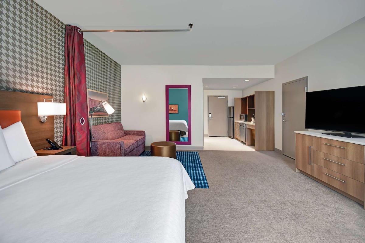 Habitación de hotel con una cama grande, un escritorio con lámpara, televisión y baño visible a través de una puerta abierta.