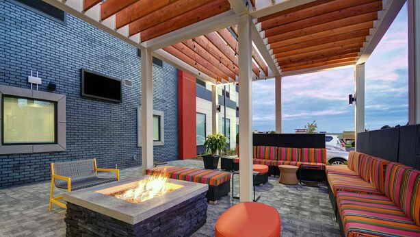An outdoor patio with a fire pit, seating, and a TV mounted on the wall.