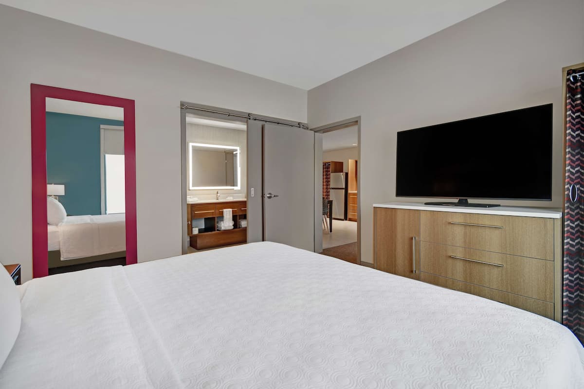 Habitación de hotel con una cama grande, televisión, armario y baño visible a través de una puerta abierta.