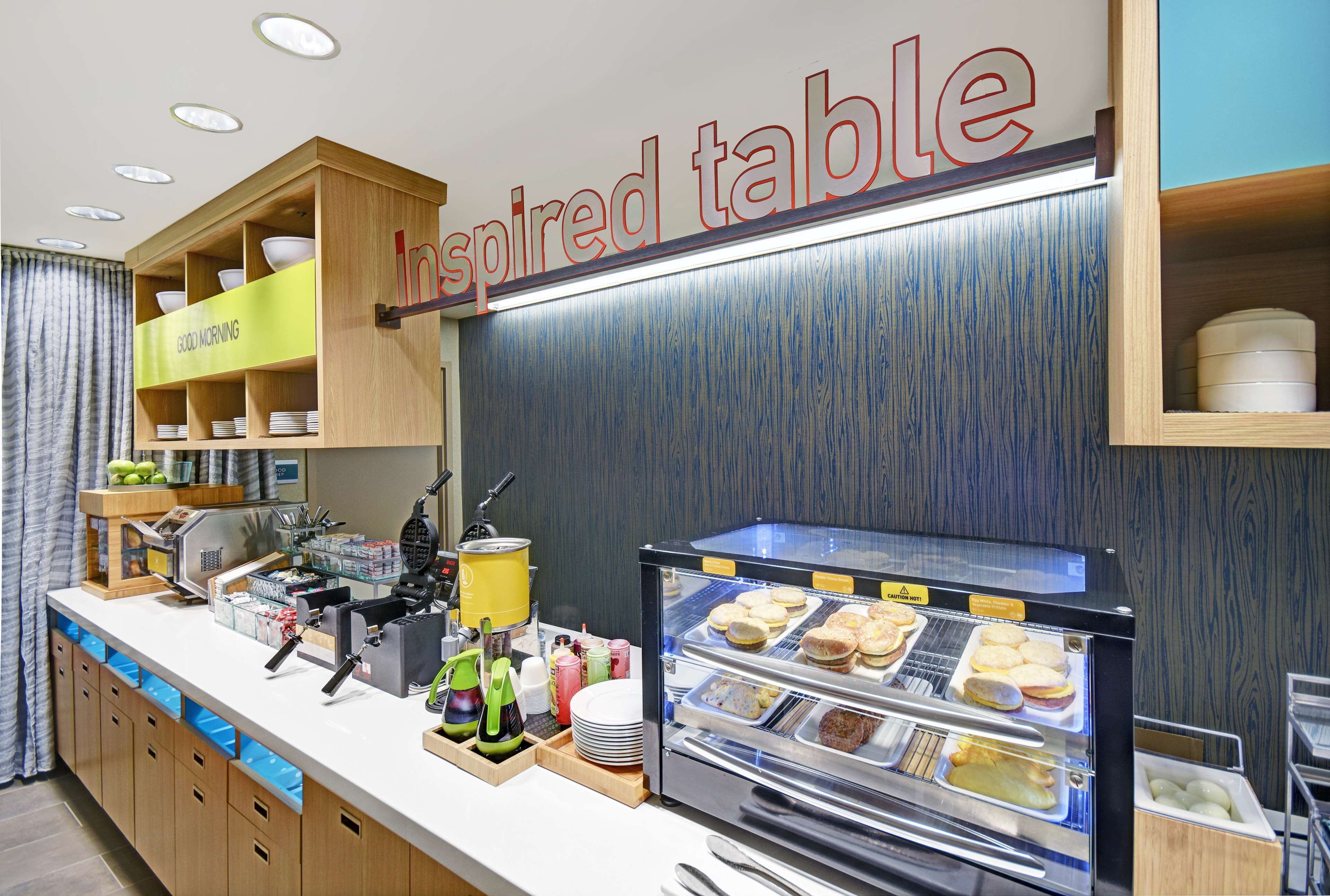 A breakfast bar with a display case of pastries and a sign reading "Inspired table".