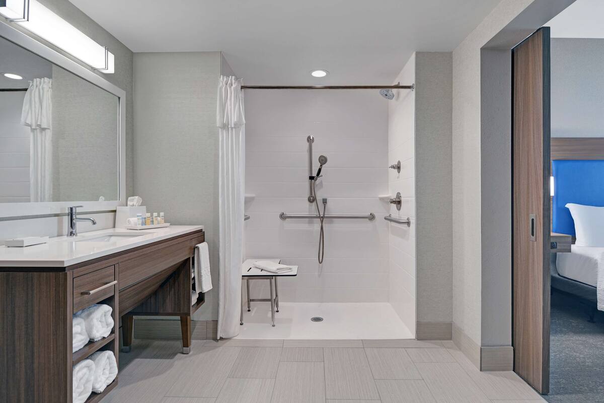 A modern bathroom with a walk-in shower, a vanity with a mirror, and a small table with towels.