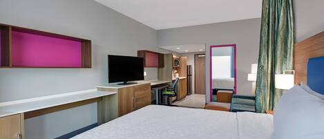 A hotel room with a bed, a desk, a television, and a bathroom visible through an open door.