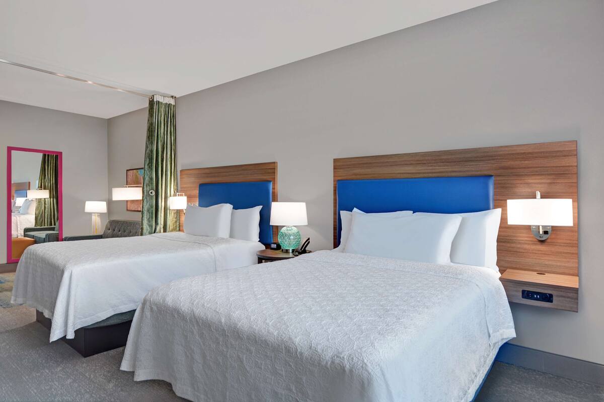 A hotel room with two beds, a large mirror, a green curtain, and a wooden headboard.