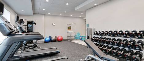 A gym with treadmills, exercise balls, and a rack of dumbbells.