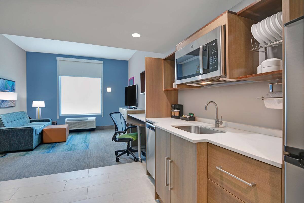 A modern kitchen with stainless steel appliances, a built-in microwave, and a sink. There is a dining area with a blue sofa and a small table.