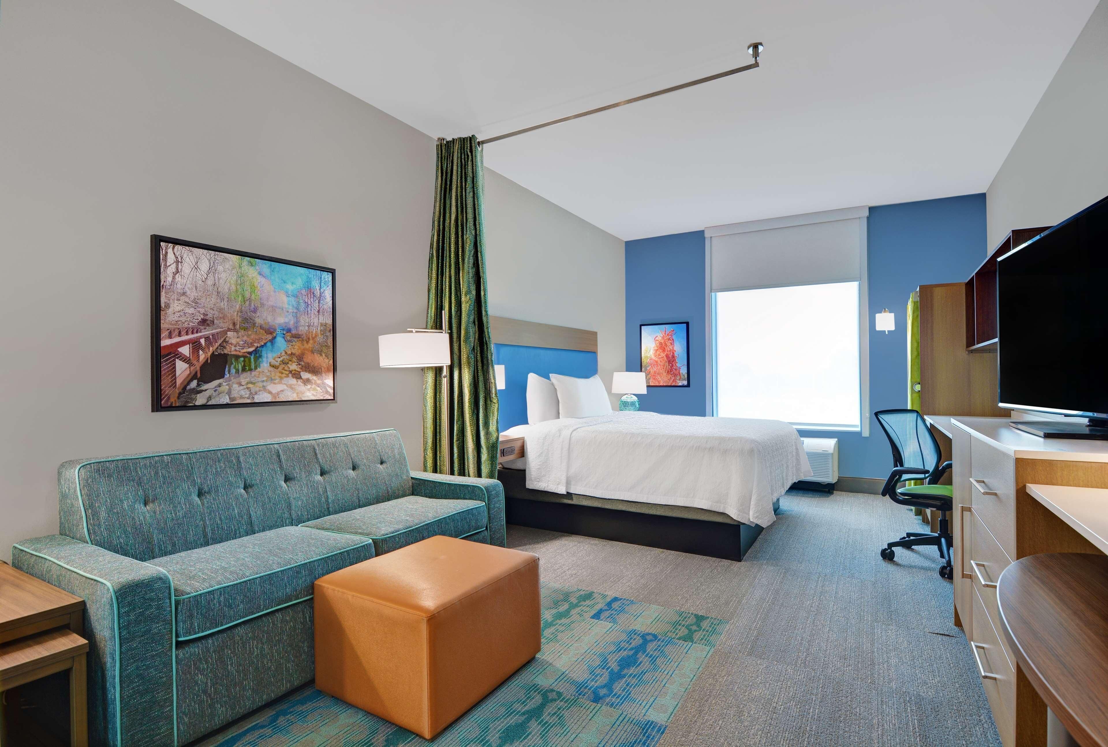 Une chambre d’hôtel avec un canapé, un lit, un bureau et un tableau au mur.