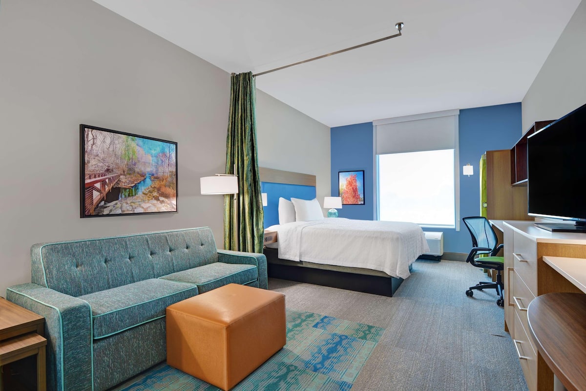Une chambre d’hôtel avec un canapé, un lit, un bureau et un tableau au mur.