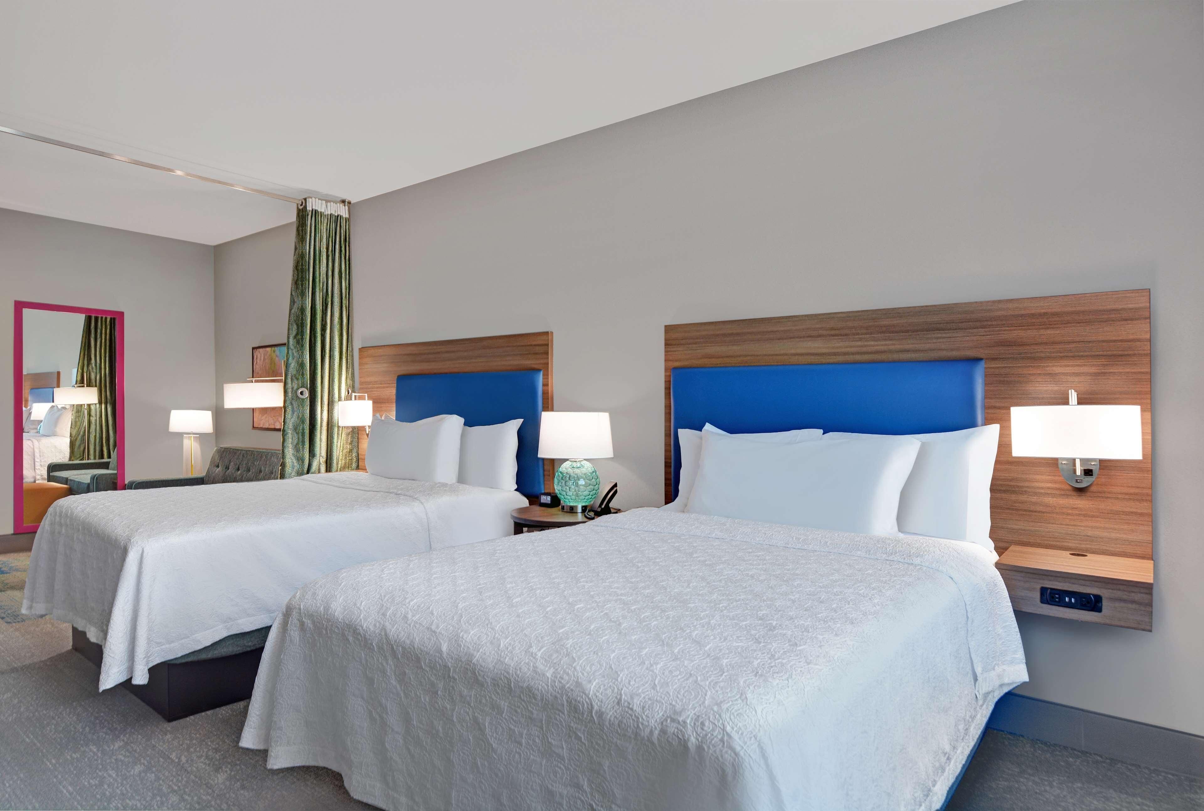 Une chambre d’hôtel avec deux lits, une table de chevet avec une lampe, un miroir et un rideau vert.