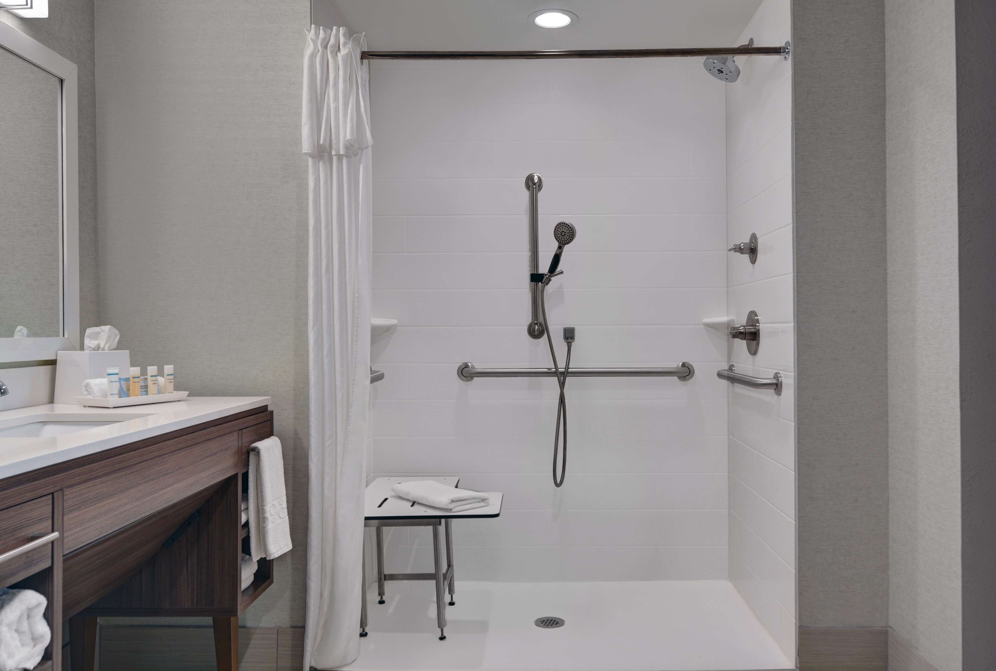 Ein modernes Badezimmer mit Dusche, Waschtisch mit Pflegeartikeln und einem kleinen Tisch mit Handtuch.