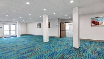 Una habitación amplia con alfombra estampada, pilares blancos y una puerta que da al exterior.