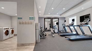 Un gimnasio moderno con bicicletas estáticas, cintas de correr y una zona de lavandería.
