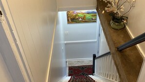A staircase with a red carpet, white walls, and a painting above the top landing. - Cozzy Get Away Priv. Apt/ St BarnabaS Hosp/NYC/EWR (Livingston)