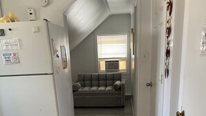 A narrow hallway with a kitchenette on the left, a gray sofa in the center, and a door on the right. - Cozzy Get Away Priv. Apt/ St BarnabaS Hosp/NYC/EWR (Livingston)