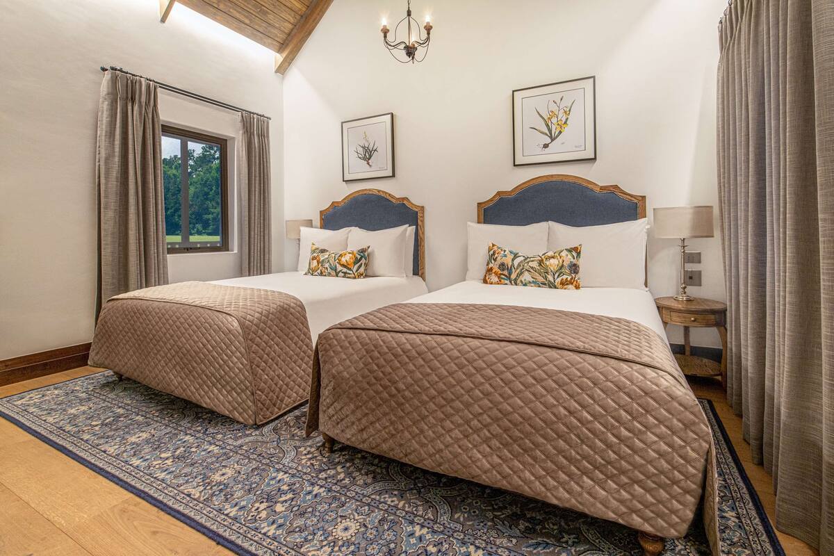 A double room with two beds, a large window, and a chandelier.