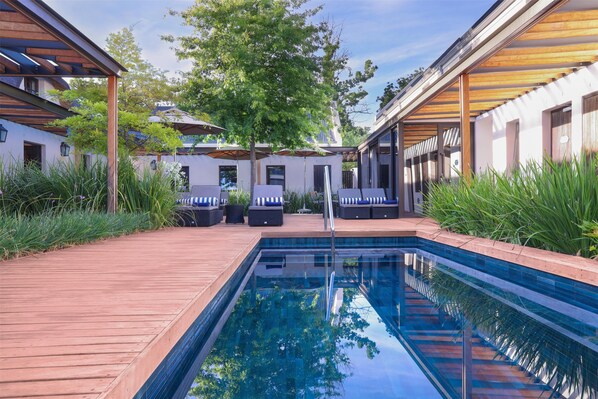 A swimming pool with wooden deck, lounge chairs, and a covered seating area with umbrellas. - Southern Sun de Wagen (Stellenbosch)