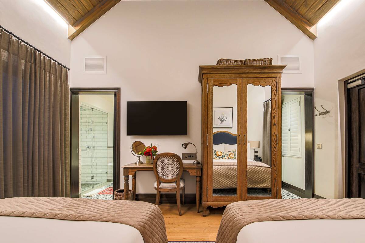 A bedroom with two beds, a desk with a chair, a television, and a wooden cabinet.