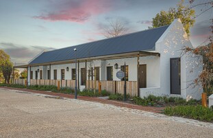 A modern building with a sloped roof, a wooden fence, and a gravel pathway leading to the entrance.