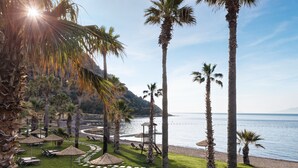 A resort with a beach view, palm trees, and lounge chairs. - Radisson Collection Hotel Bodrum (Bodrum)