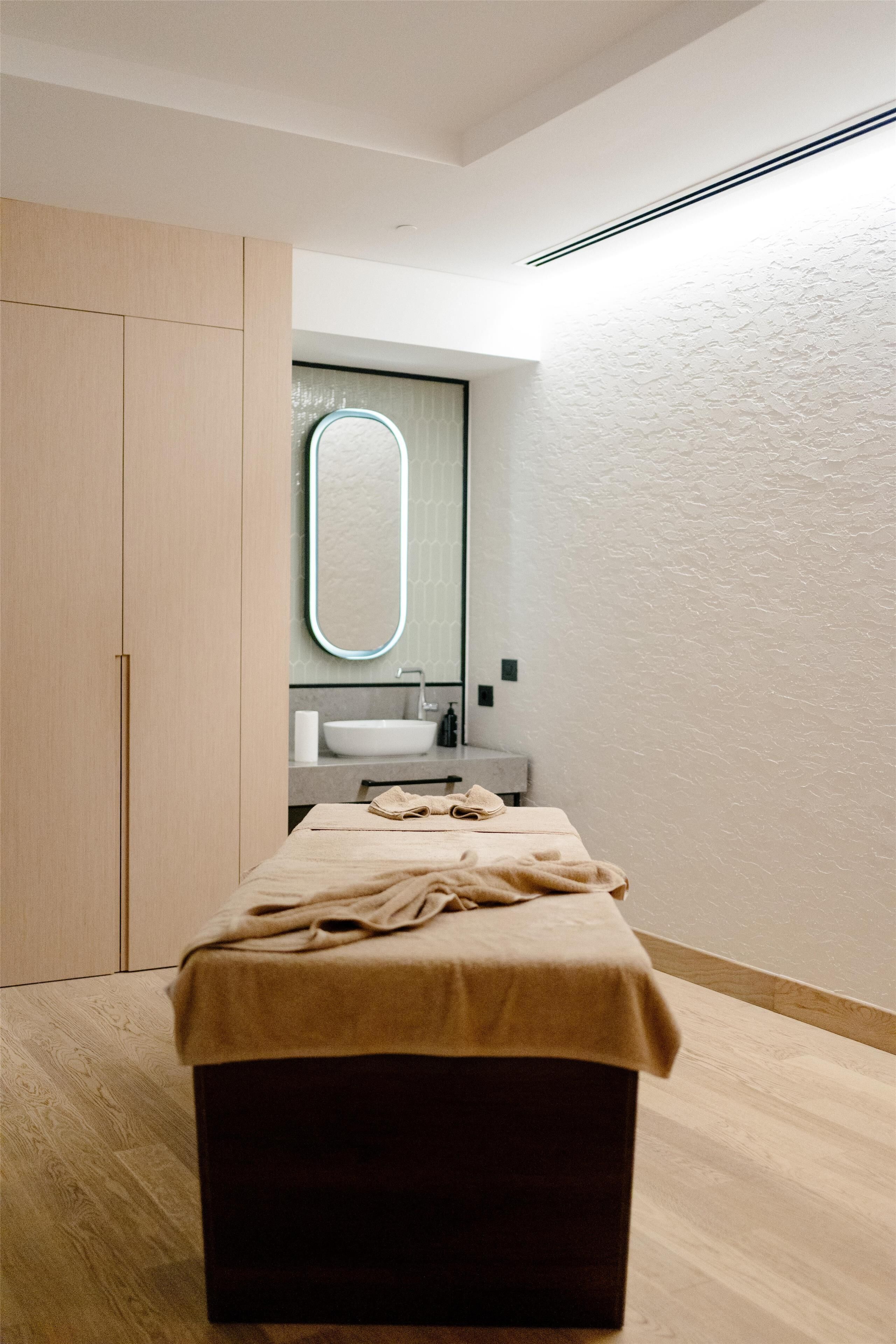 A modern bedroom with a wooden wardrobe, a large mirror, a bed with a beige blanket, and a wooden floor.