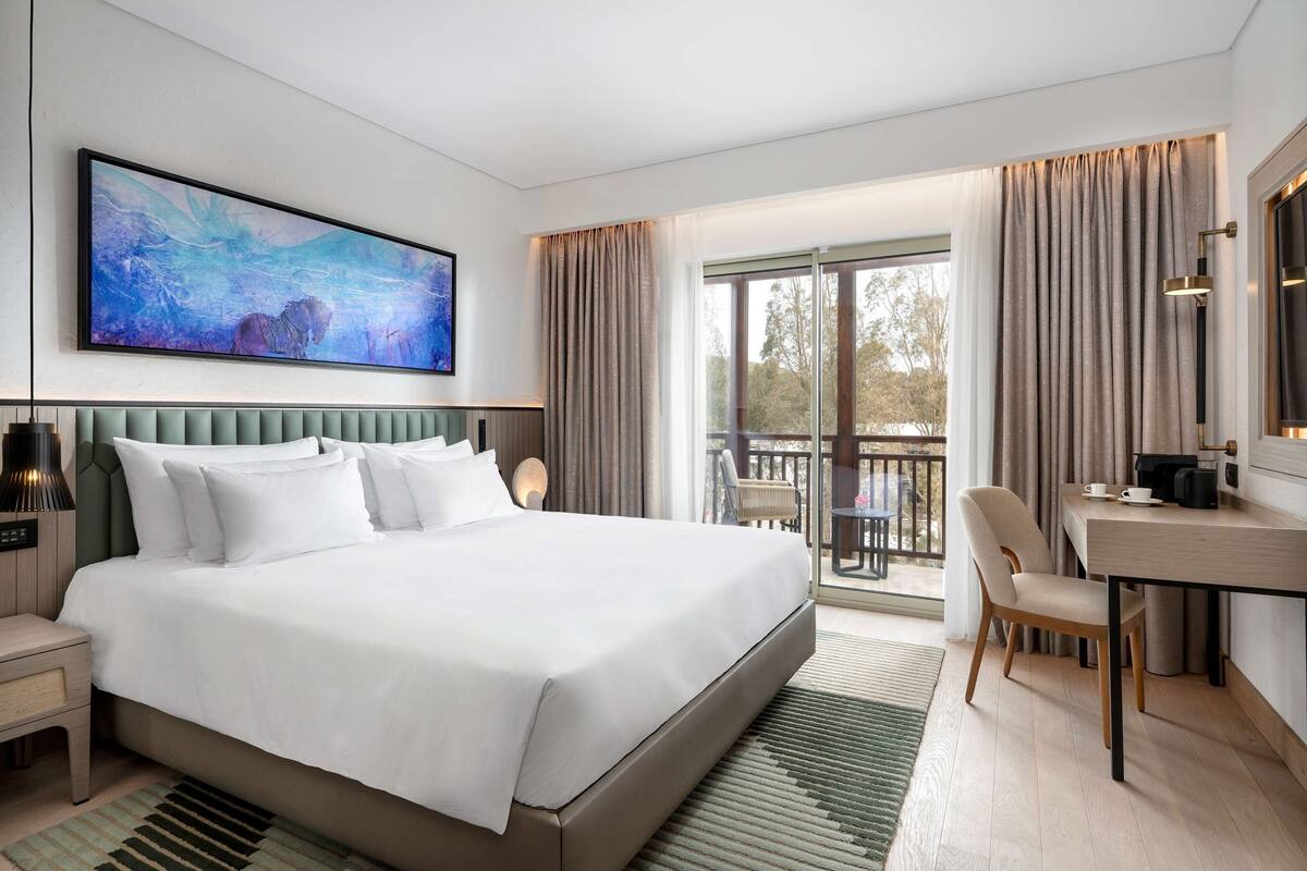 Una habitación de hotel moderna con una cama grande, un escritorio y un balcón con vistas.