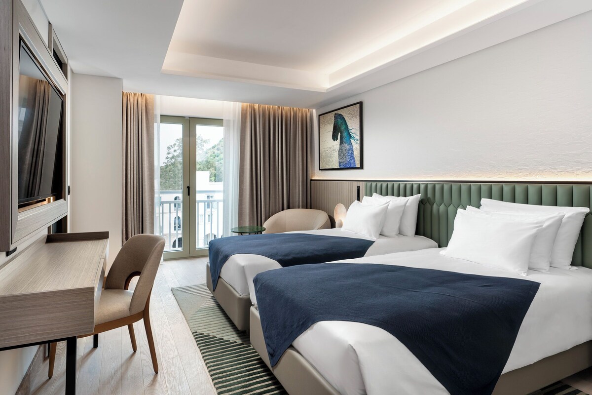 A hotel room with two beds, a desk, and a TV.