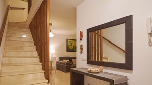 Un escalier avec des rampes en bois, une console sombre agrémentée d’un miroir et un canapé dans un salon bien éclairé.