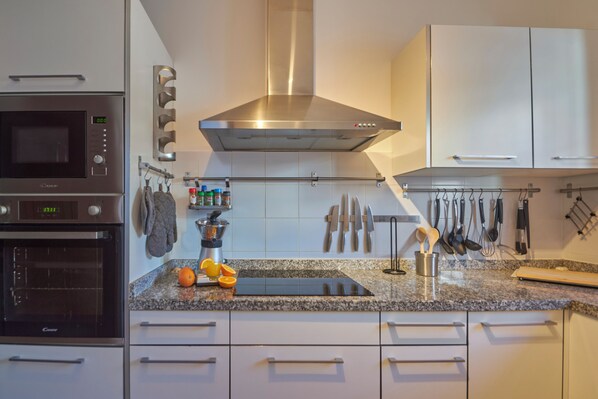 Una cocina moderna con electrodomésticos de acero inoxidable, encimera de granito y varios utensilios colgando en la pared.