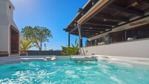 Une piscine avec un bassin aux eaux d’un bleu limpide, entourée d’une terrasse couverte offrant une vue sur le ciel et un arbre.