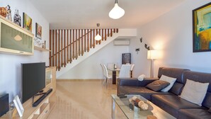 Un salon moderne avec un téléviseur à écran plat, une table basse en verre, un canapé en cuir et un escalier.