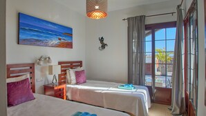 Une chambre d’hôtel avec deux lits, un tableau représentant une plage, un élément décoratif mural et une vue par la fenêtre.
