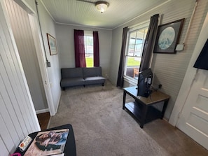 Una habitación con sofá, televisor sobre un mueble bajo, un cuadro en la pared y una puerta que da al exterior.