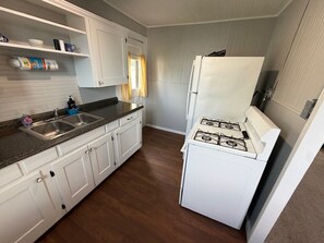 Una cocina compacta con armarios blancos, un lavamanos doble, una estufa a gas y un refrigerador.