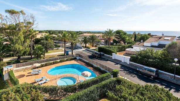 Une grande piscine avec des chaises longues et un petit jacuzzi, le tout entouré d’une végétation luxuriante et offrant une vue sur la mer.