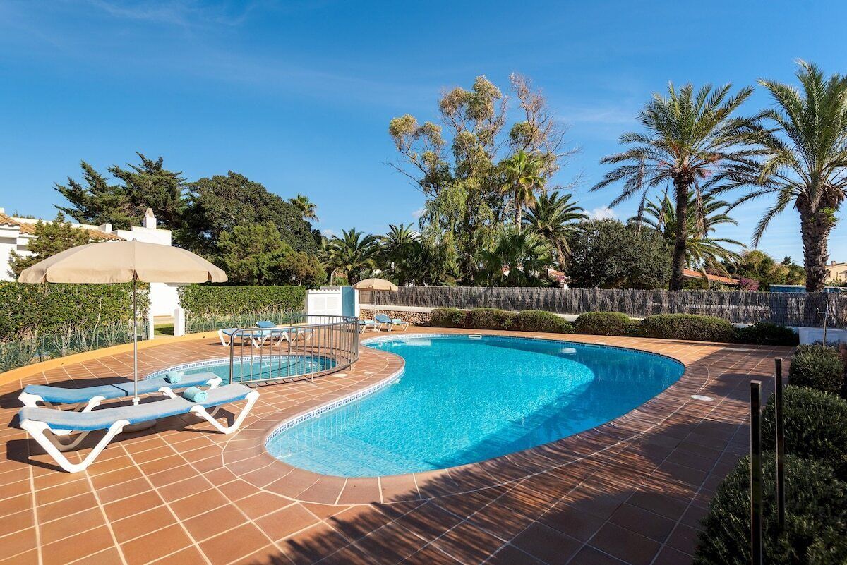 A swimming pool with sun loungers and a tiled deck.