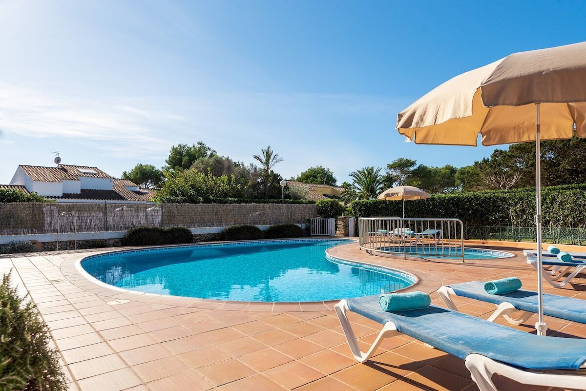 Ein Swimmingpool mit Liegestühlen und Sonnenschirmen, umgeben von einer gefliesten Terrasse und einer Steinmauer.