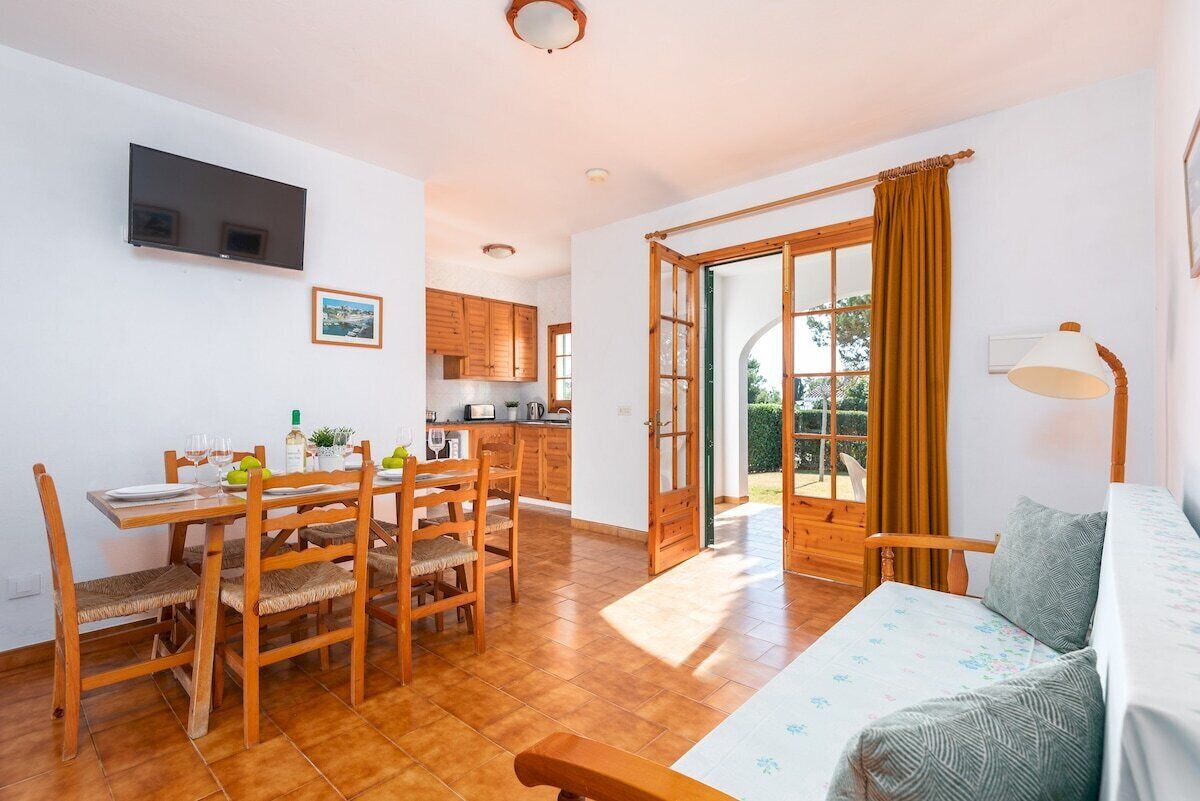 A cozy room with a wooden dining table, chairs, a sofa, and a TV mounted on the wall.