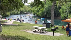 A riverside park with picnic tables, a trash bin, and a covered area.