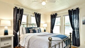 A bedroom with a bed, bedside tables, a ceiling fan, and windows with curtains.