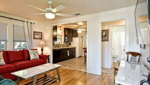 A spacious living area with a red sofa, a wooden coffee table, and a dining table with chairs. There is a kitchen in the background with a refrigerator and a microwave.