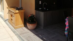 An outdoor kitchen area with a wooden counter, a sink, and a large planter with red flowers. - Charming independent studio in Martigues town center, swimming pool, spa (Martigues)