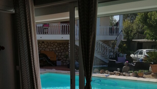 A room with a view of a swimming pool, a balcony with a stone wall, and a parked car outside. - Charming independent studio in Martigues town center, swimming pool, spa (Martigues)